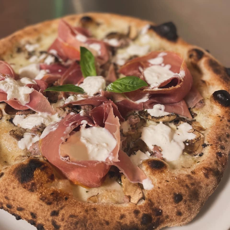 Pizza cotta nel forno a legna con prosciutto crudo, mozzarella, basilico e scaglie di formaggio.