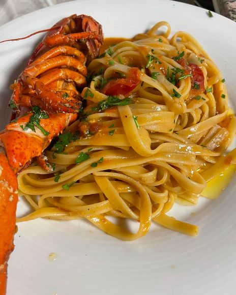 Coda di aragosta con fettuccine in salsa leggera su un piatto bianco.