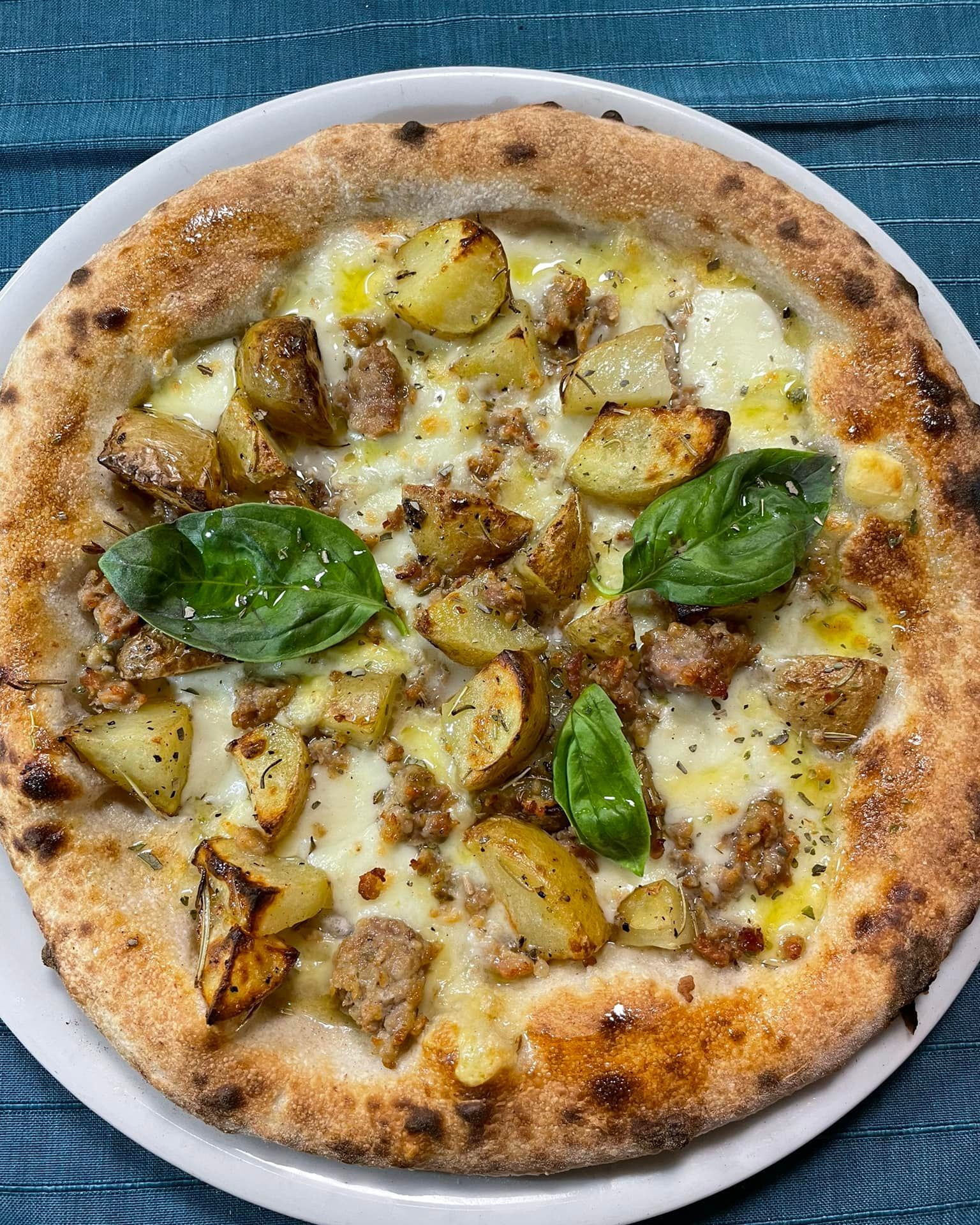 Pizza Margherita con foglie di basilico, patate arrosto e formaggio fuso su un piatto bianco.