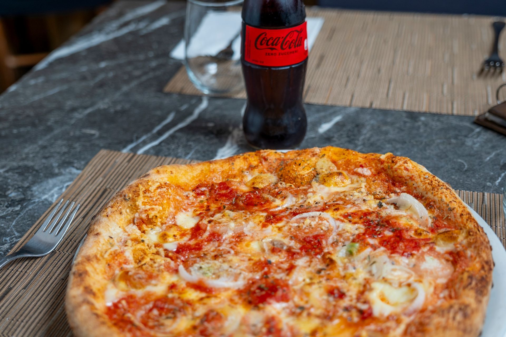 Primo piano di una pizza al formaggio con la crosta bruciacchiata su un piatto bianco.