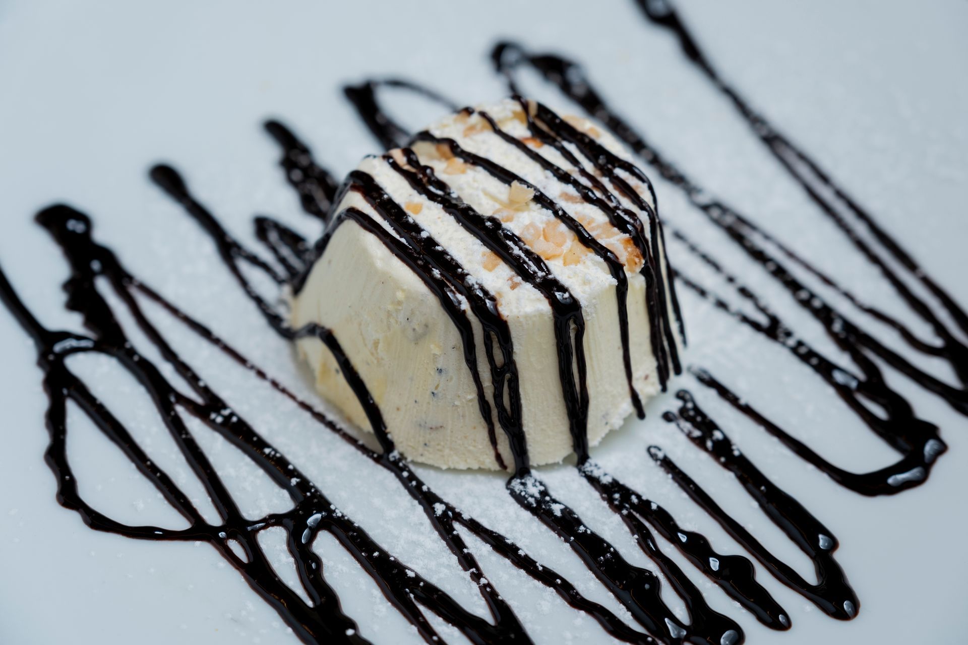 Dessert servito su un piatto bianco con gelatina di mango, salsa scura e guarnizioni.