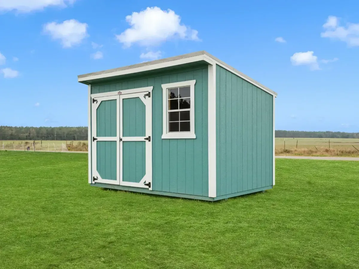Small teal shed with white trim and double doors on a grassy field under a blue sky