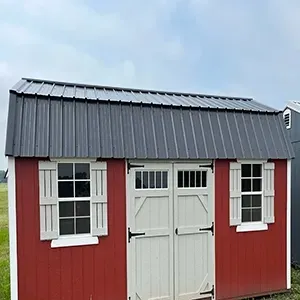 Red shed with gray metal roof and white double doors and windows against a cloudy sky
