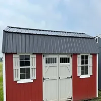 Red shed with gray metal roof and white double doors and windows against a cloudy sky