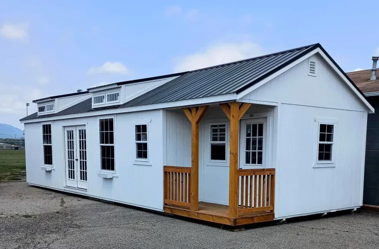 White modular house with a small porch and gray roof on a gravel lot under a cloudy sky