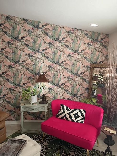 Pink chair in a floral wallpapered room with a mirrored side table and decor.