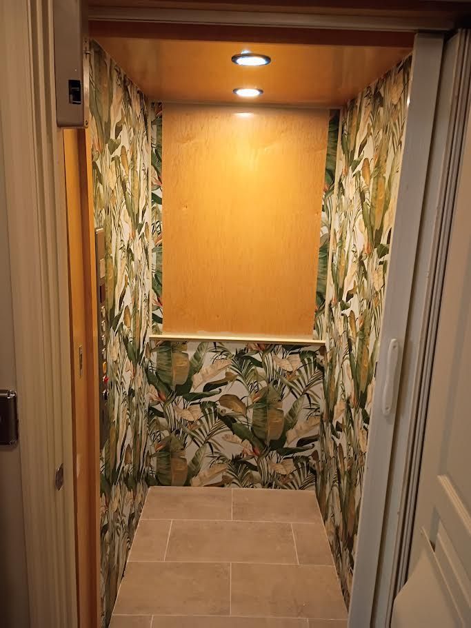 Small tiled alcove with tropical-pattern wallpaper, wood ceiling, and recessed lights, viewed through a doorway