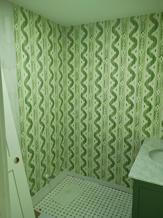 Small bathroom with green patterned shower curtain, white shower mat, and a green sink cabinet.
