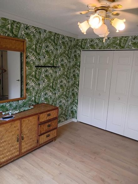 Empty bedroom with green patterned wallpaper, white closet doors, a dresser, and a ceiling fan.