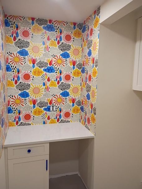 Small laundry nook with colorful patterned wallpaper, countertop, cabinet, and open shelving nook