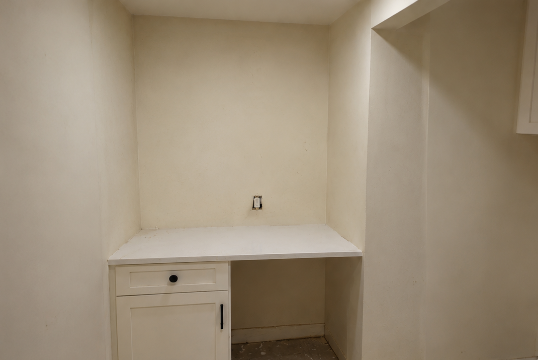 Small beige built-in desk nook with white countertop and cabinet in an empty room