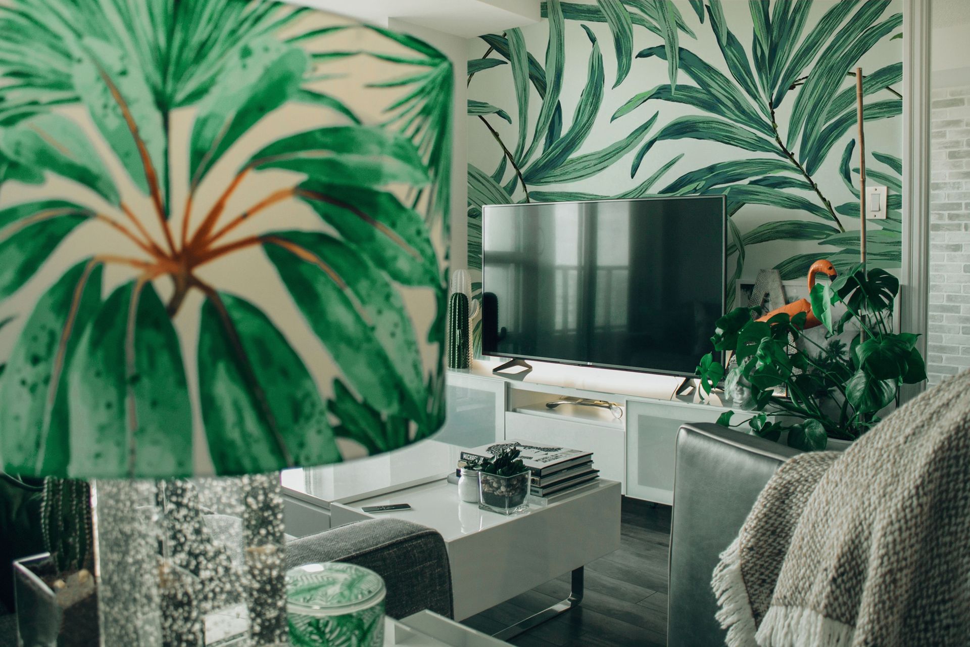 Living room with leafy lampshade, TV, gray sofa, and green floral wallpaper
