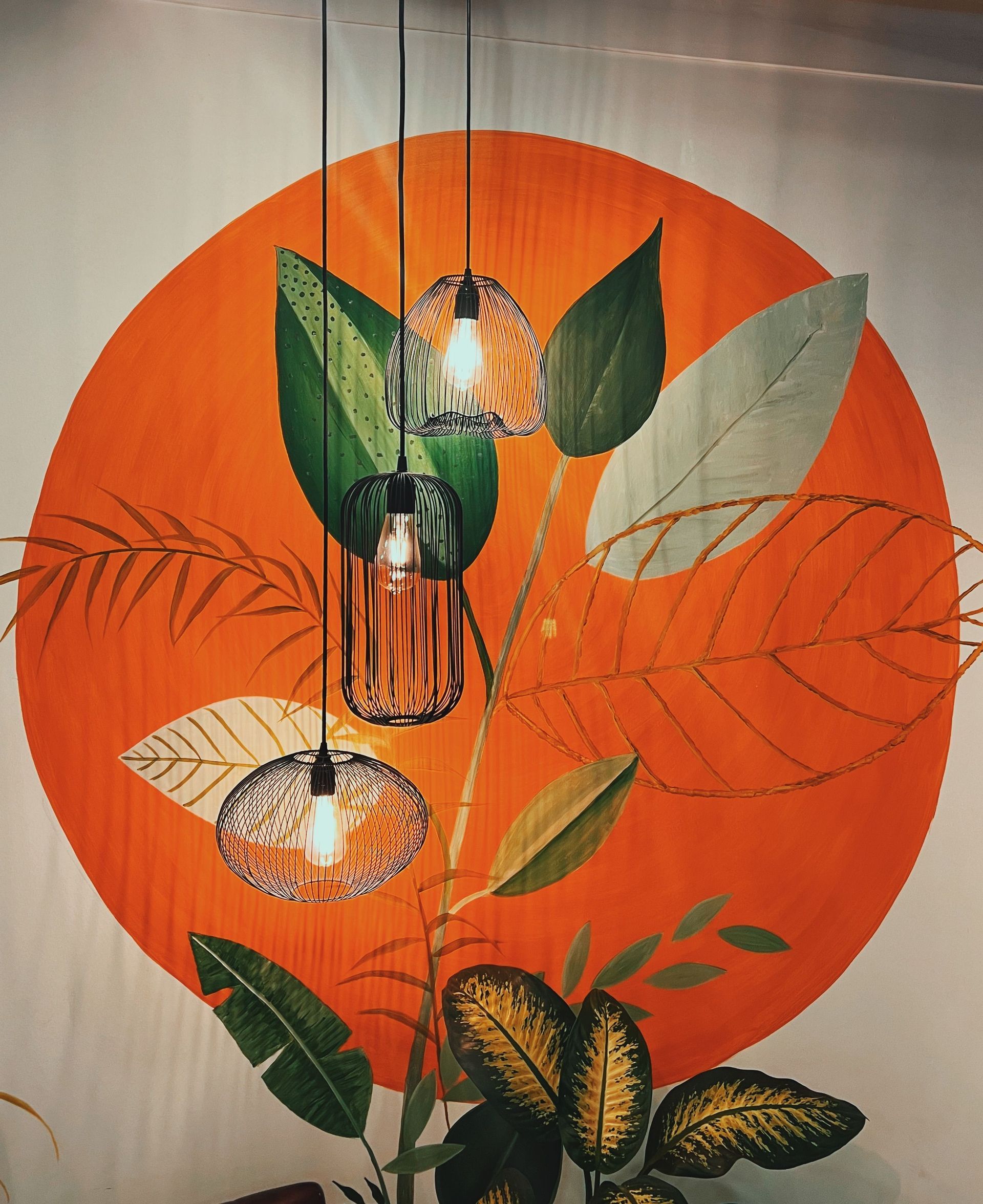 Hanging pendant lights over a mural of orange sun, green leaves, and botanical patterns