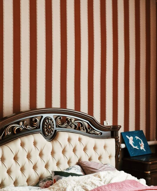 Bedroom with red-and-white striped wallpaper, a tufted cream headboard, and a blue accent pillow