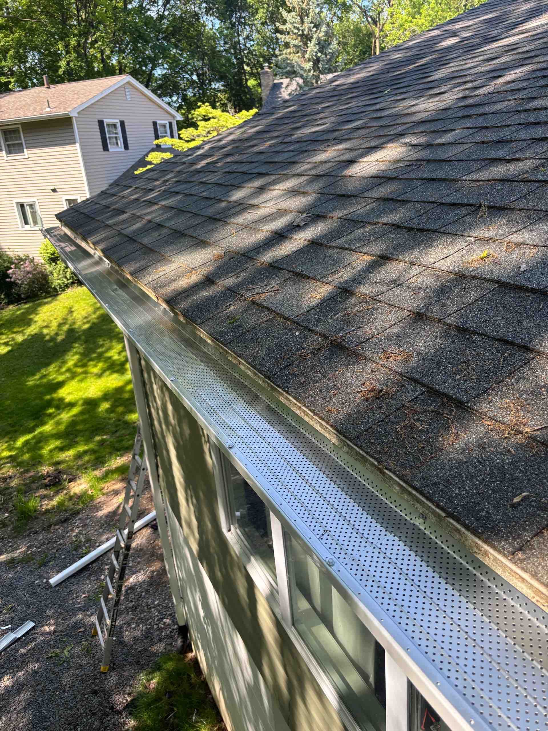 Roof edge with gray shingles above a wooden building and a white truck below on a grassy property.
