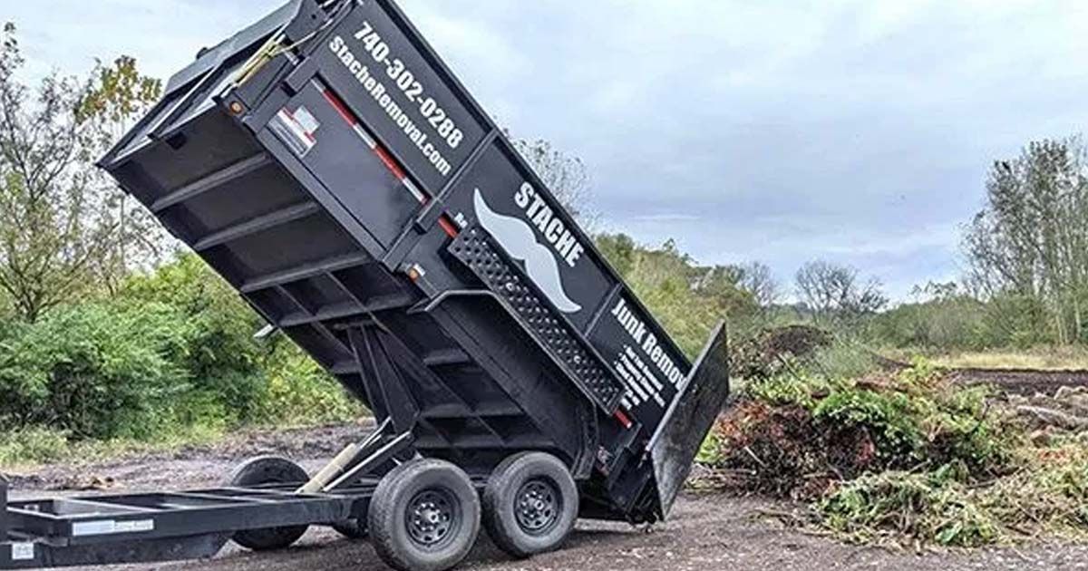 A dumpster is sitting on top of a trailer in a field.