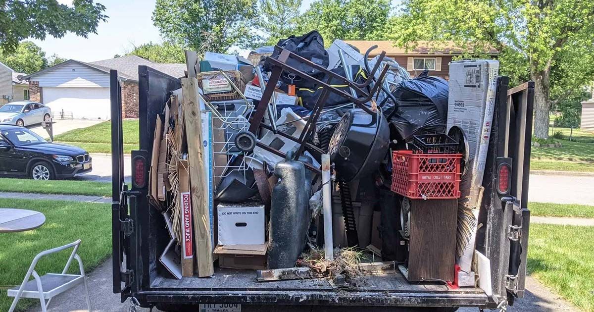 A dumpster filled with junk is parked in front of a house.