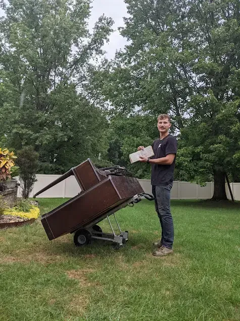 A man is standing next to a dolly with a piano on it.