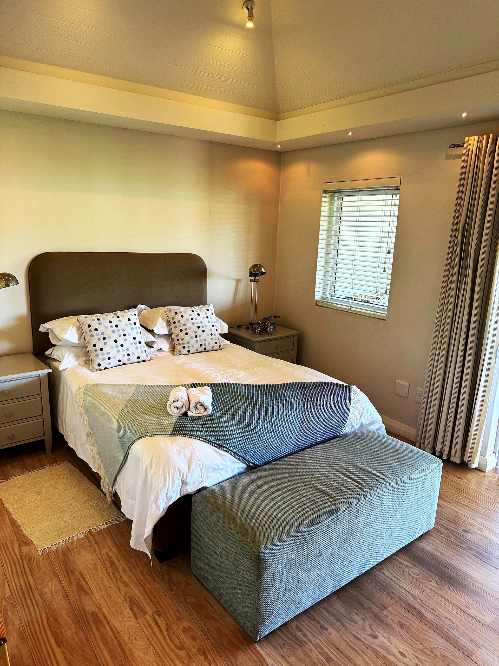 A bedroom with a bed , ottoman , nightstands and a window.