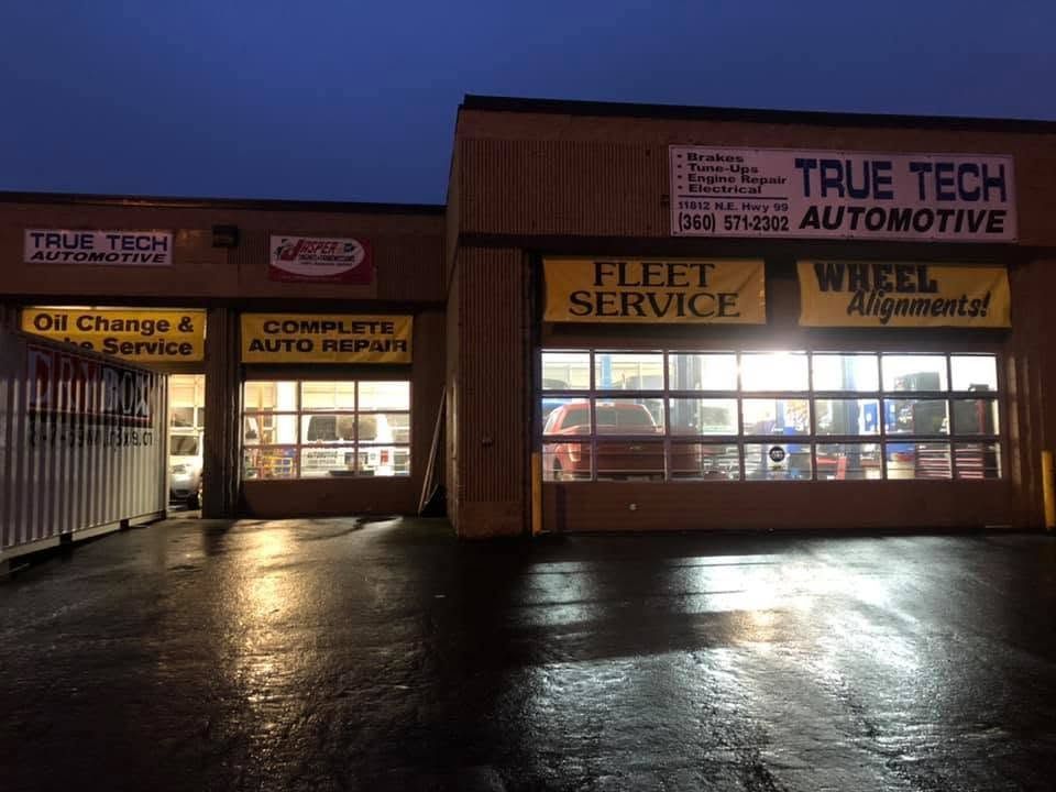 Night view of True Tech Automotive auto shop with lit windows and wet pavement reflections | TrueTech Automotive