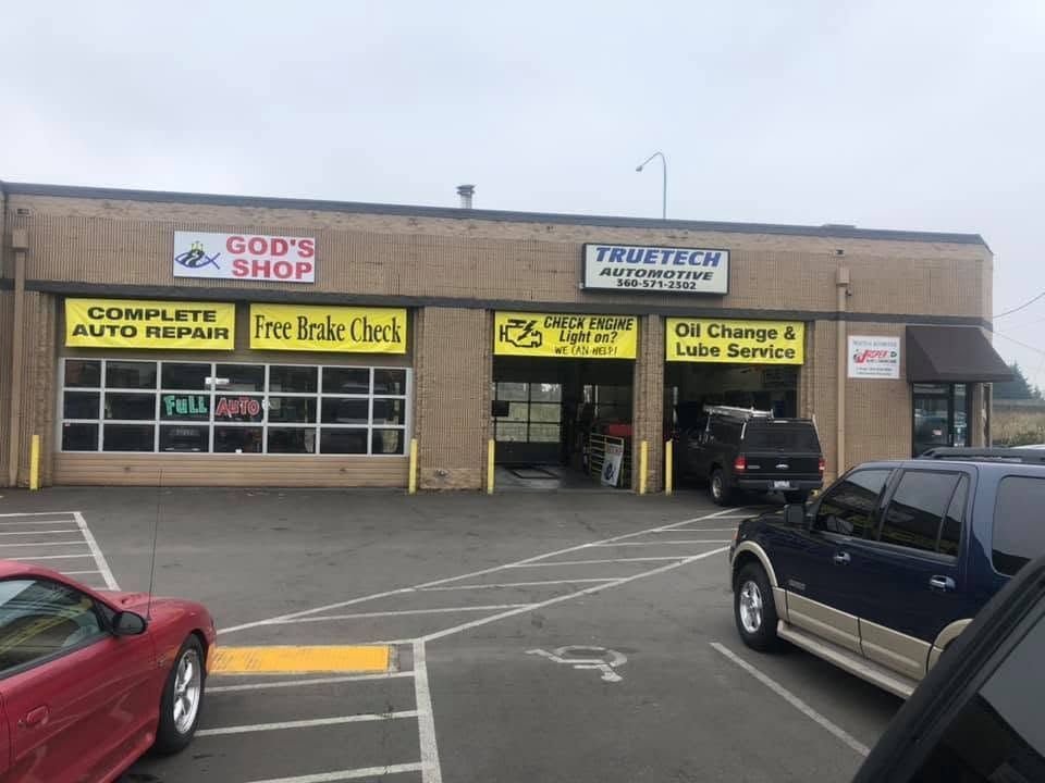 Strip mall auto repair shops with parked cars in front, including God’s Shop, The Tire Guys, and All Charged Up E-bike | TrueTech Automotive