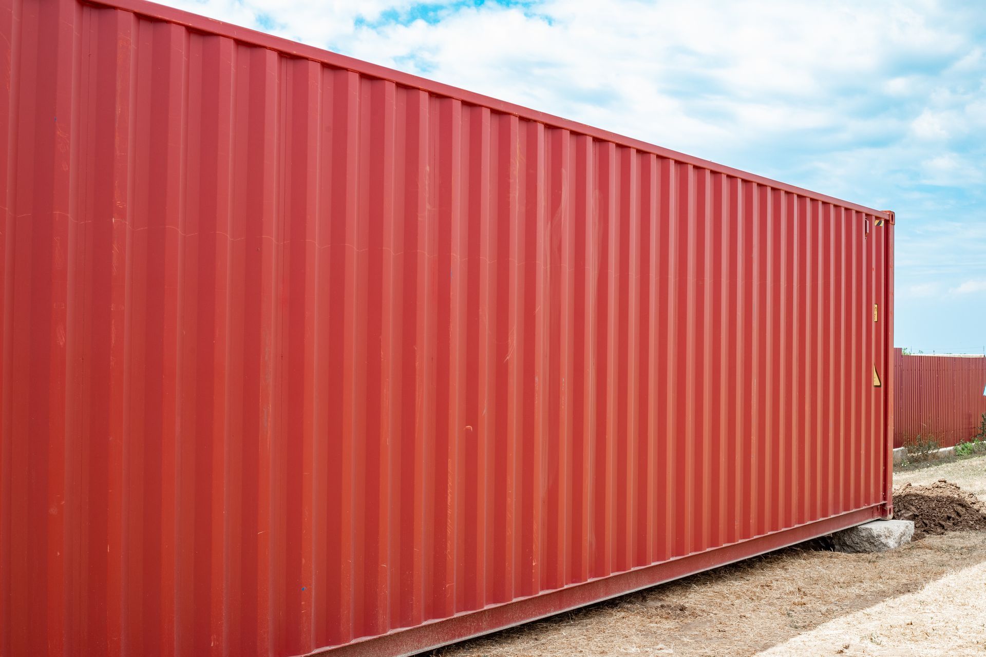 Side view of a long red corrugated shipping container on an outdoor storage site. international logi