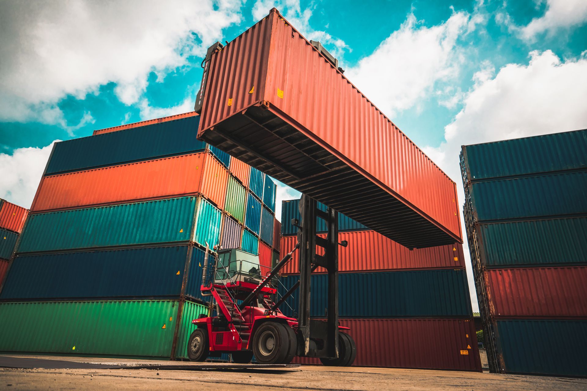 Local container supplier stacking cargo containers with forklift at industrial storage yard. Local container supplier stacking cargo containers with forklift at industrial storage yard.