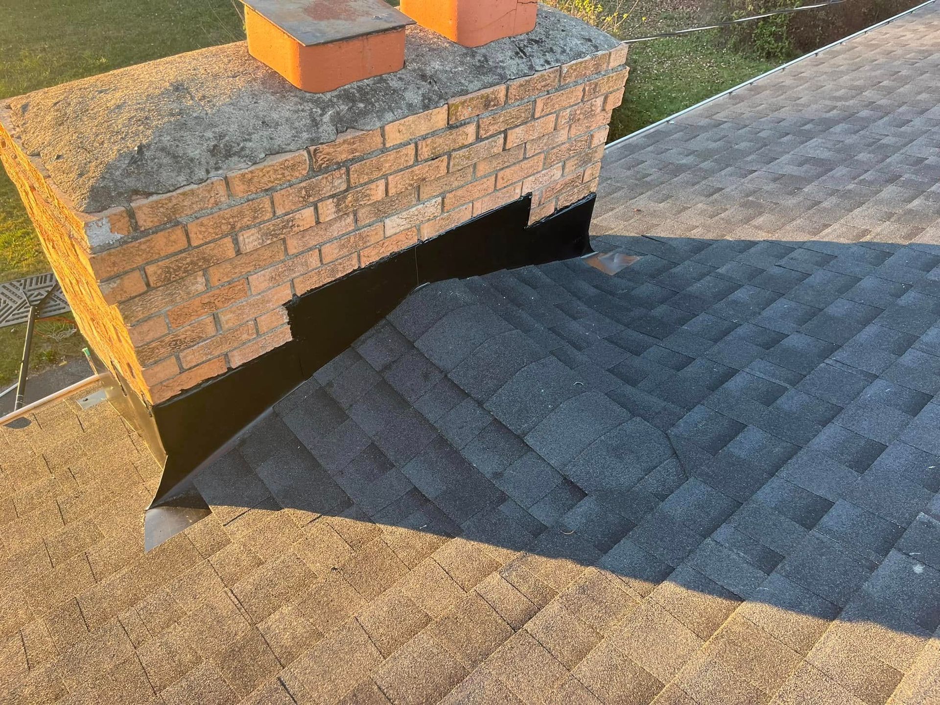A brick chimney on a sloped roof with black waterproof flashing installed along the base.