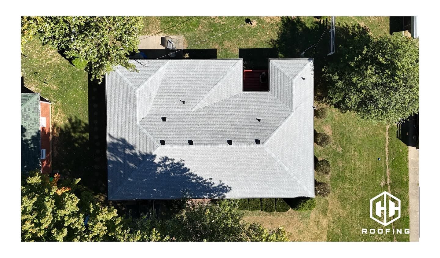 An overhead view of a light gray shingled residential roof, featuring a CC Roofing logo in the bottom right corner.