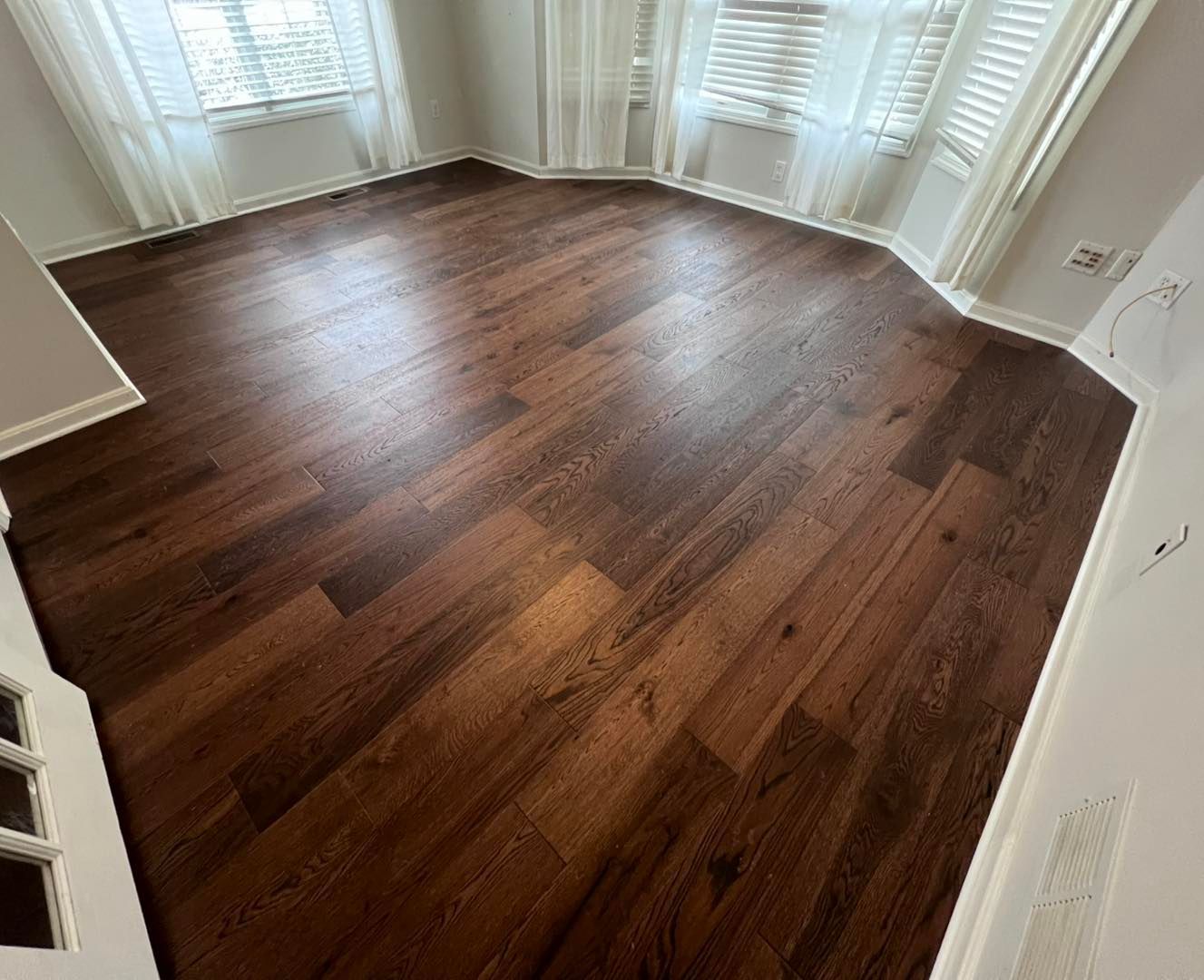 A living room with hardwood floors and white curtains.
