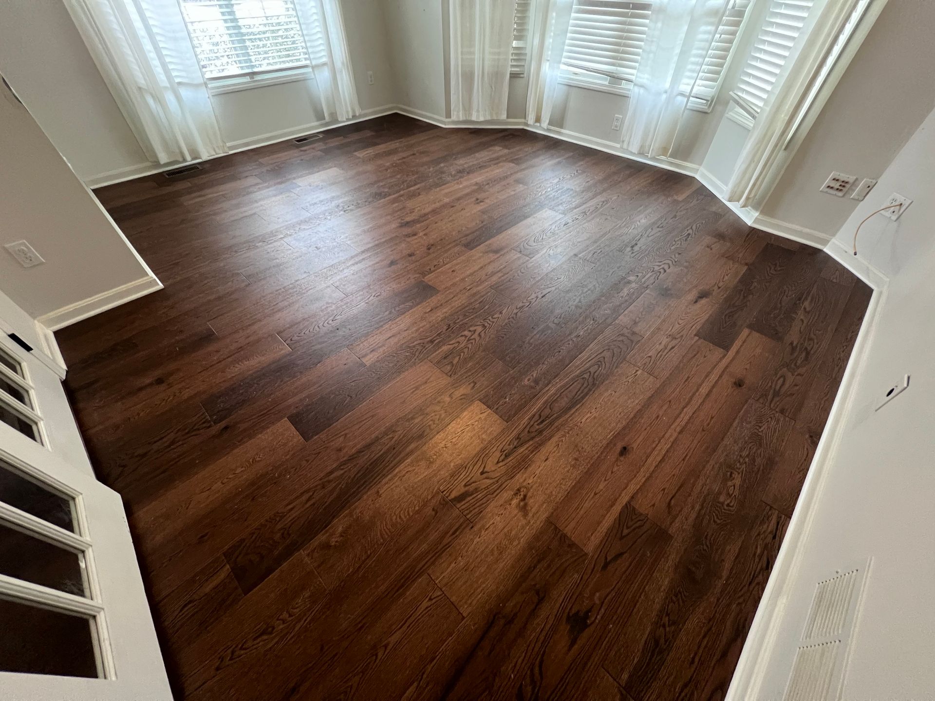 A bedroom with hardwood floors and white curtains.