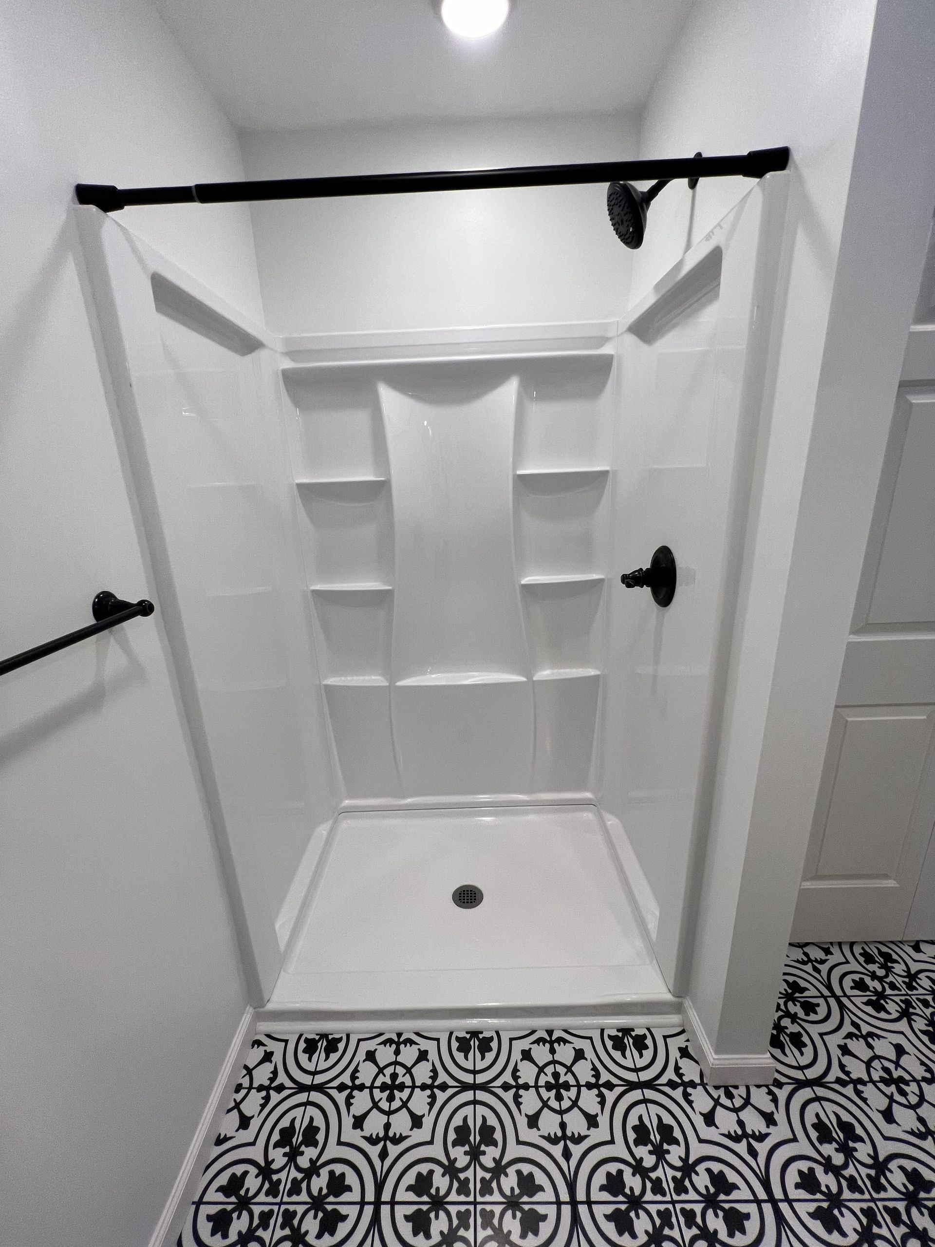 A bathroom with a walk in shower and a black and white tile floor.