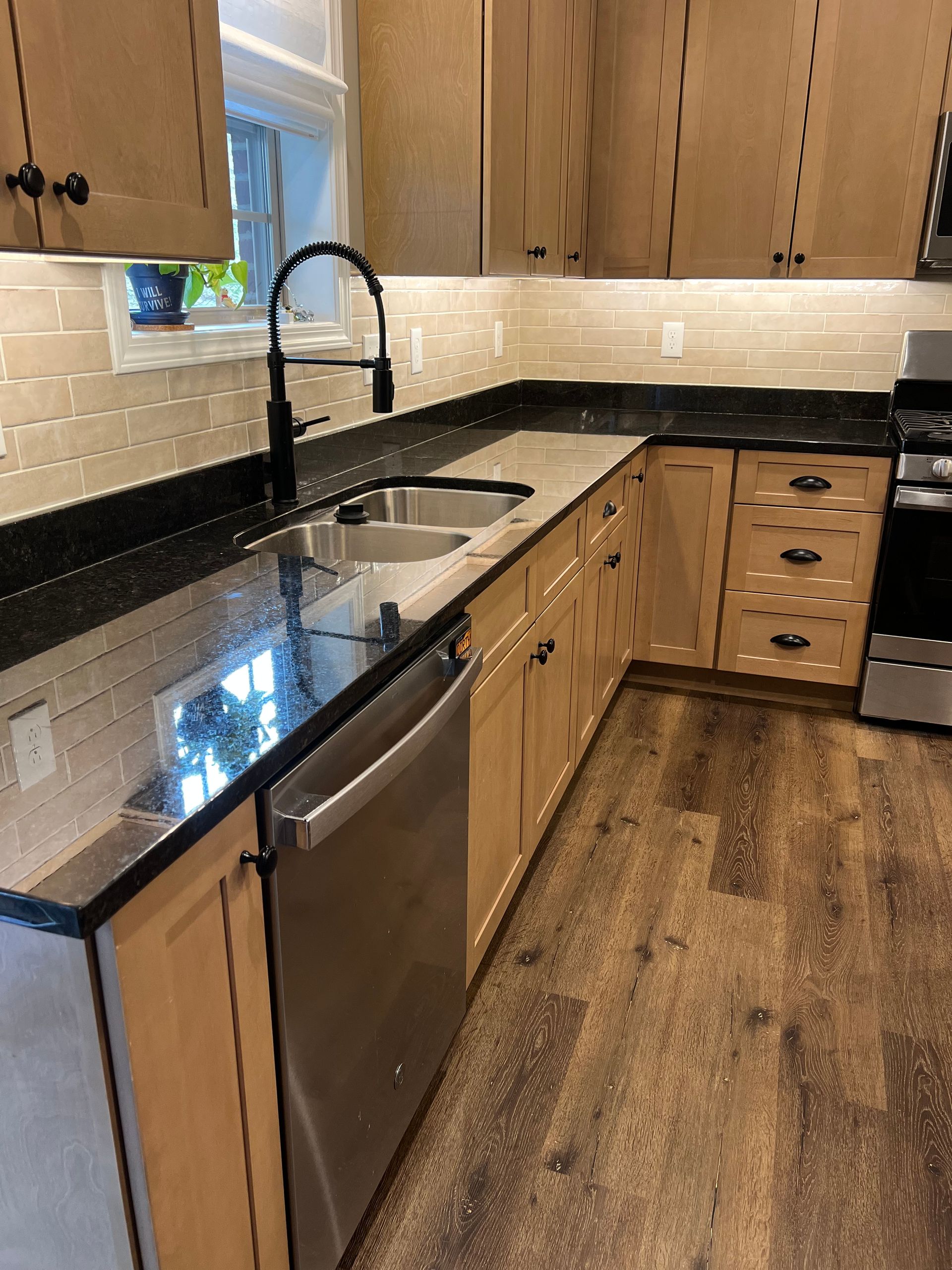 A kitchen with wooden cabinets , black counter tops , stainless steel appliances and a sink.