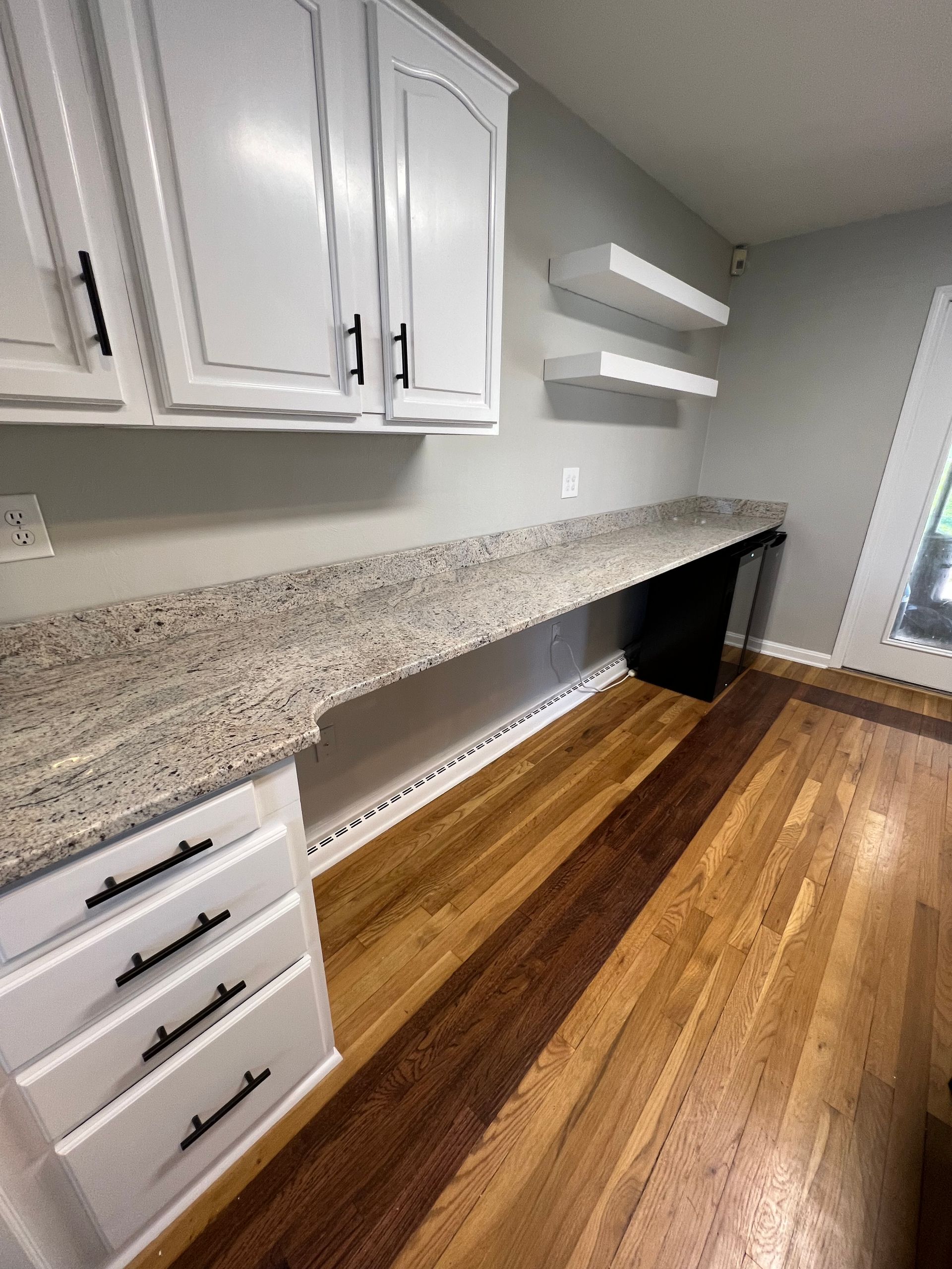 A kitchen with white cabinets , granite counter tops , and wooden floors.
