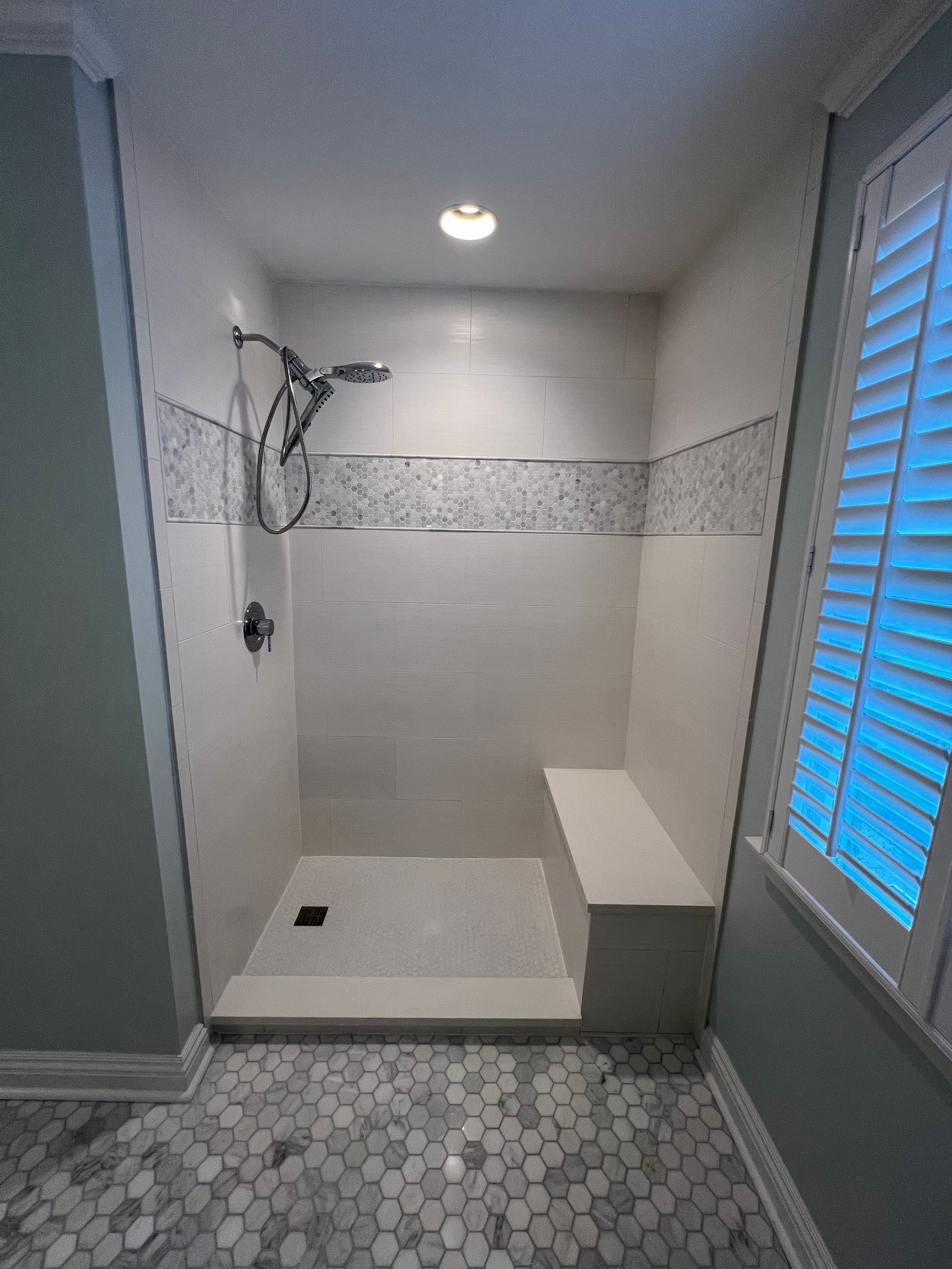 A bathroom with a walk in shower and a bench.