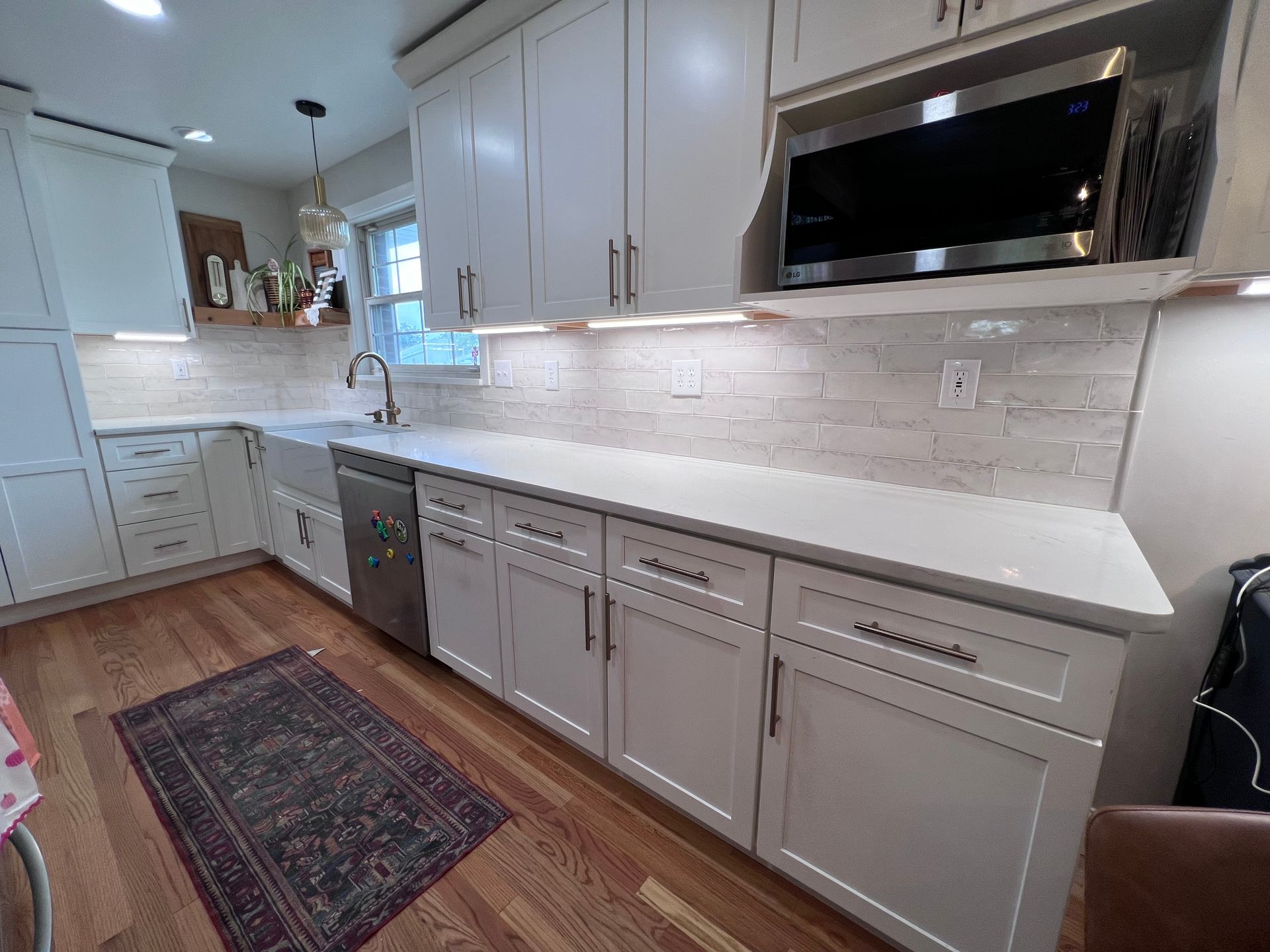 A kitchen with white cabinets , stainless steel appliances , a microwave and a rug.