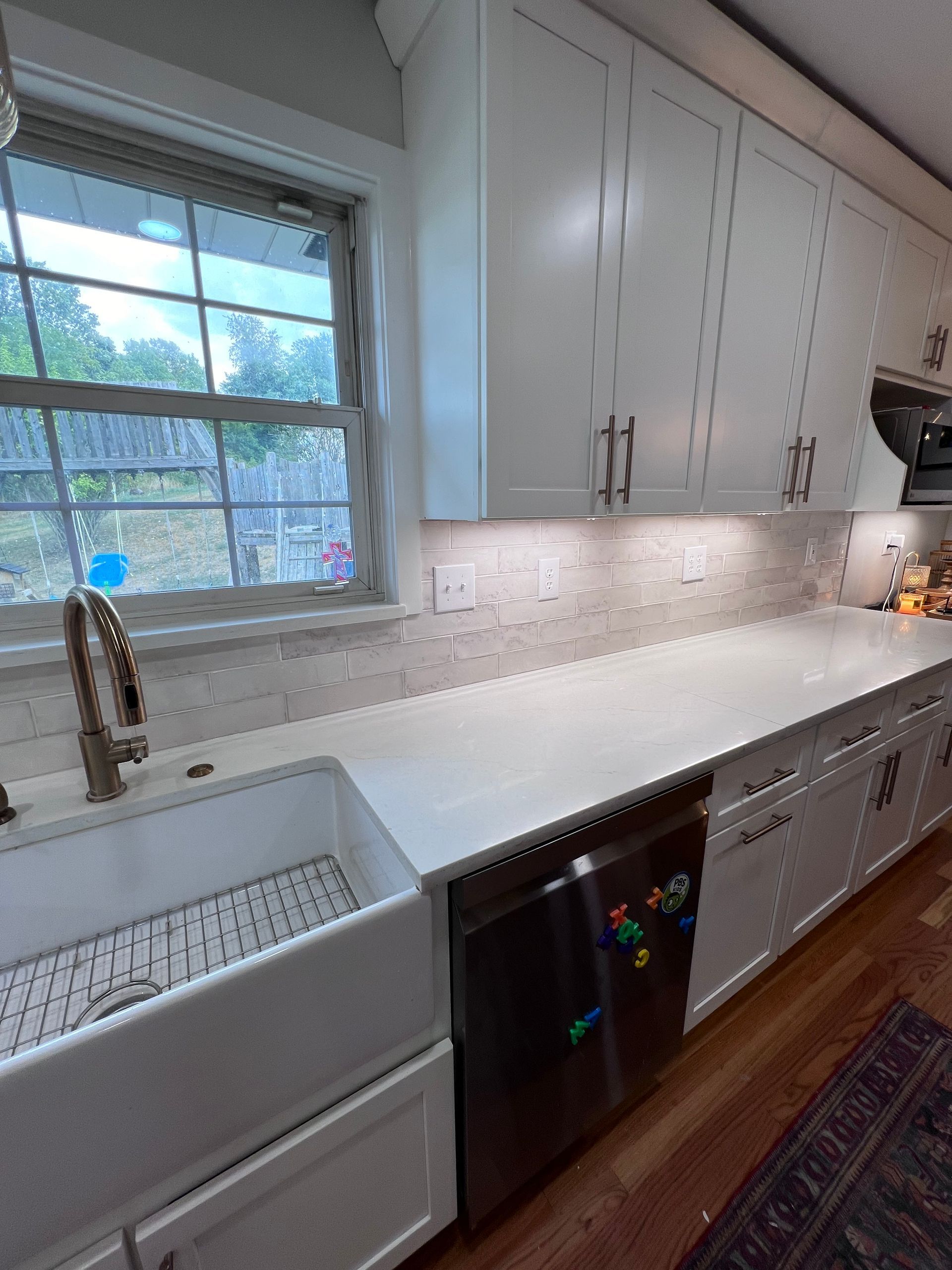 A kitchen with white cabinets , a sink , a dishwasher , and a window.
