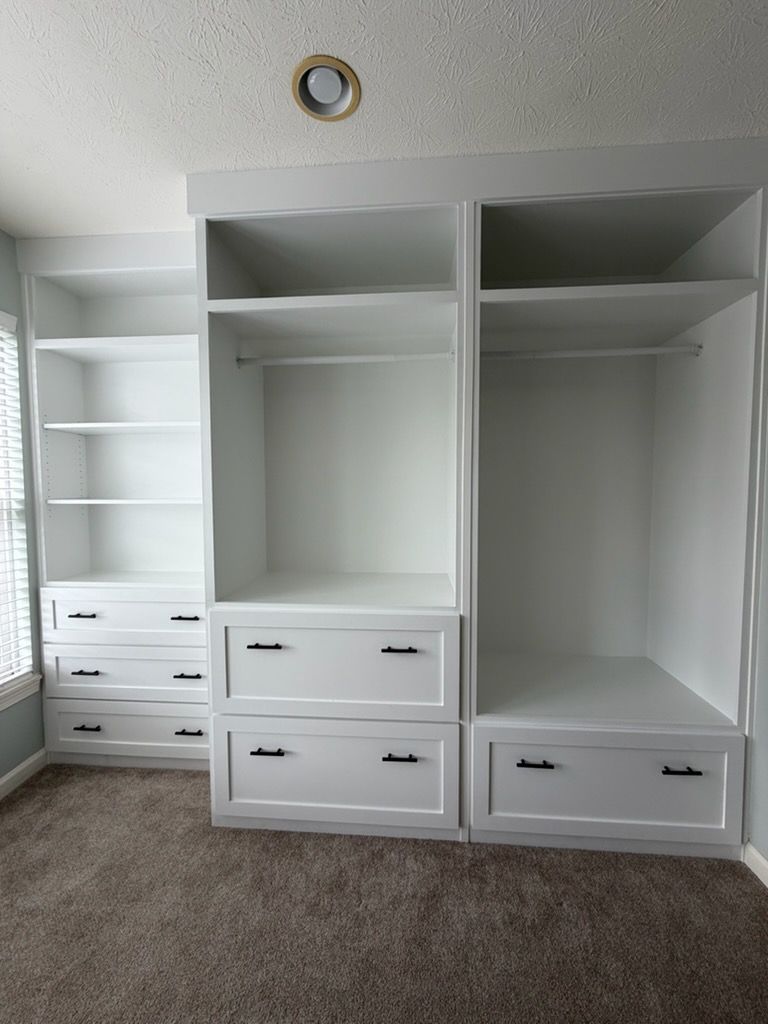 Empty bedroom with built-in white closet storage and drawers against a gray wall.