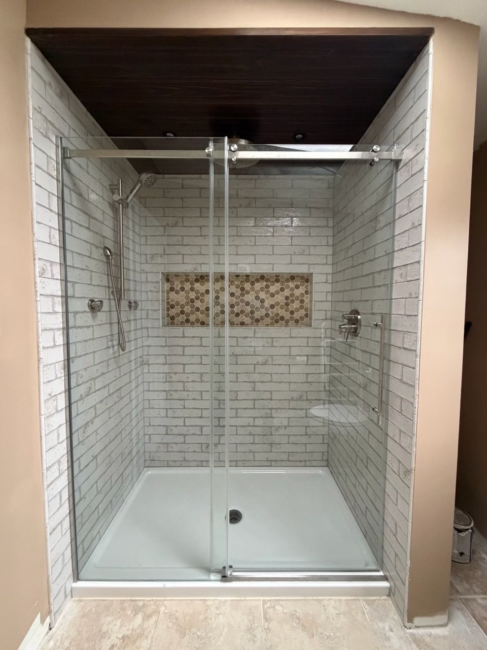 Glass-enclosed white-tiled shower with chrome fixtures and a pebble accent wall.