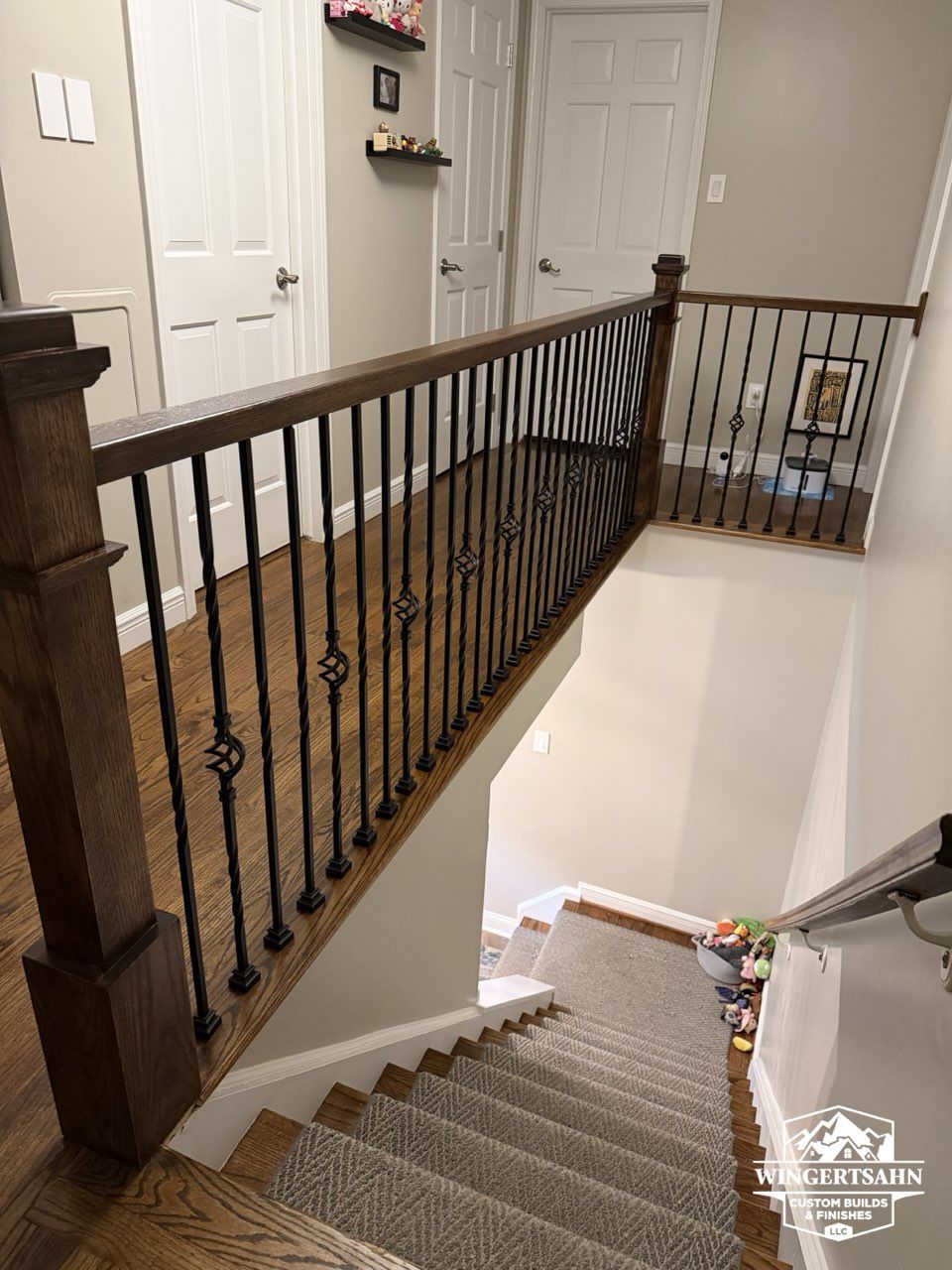 Stairwell with carpeted stairs, dark wood railing, and a landing hallway with white doors.