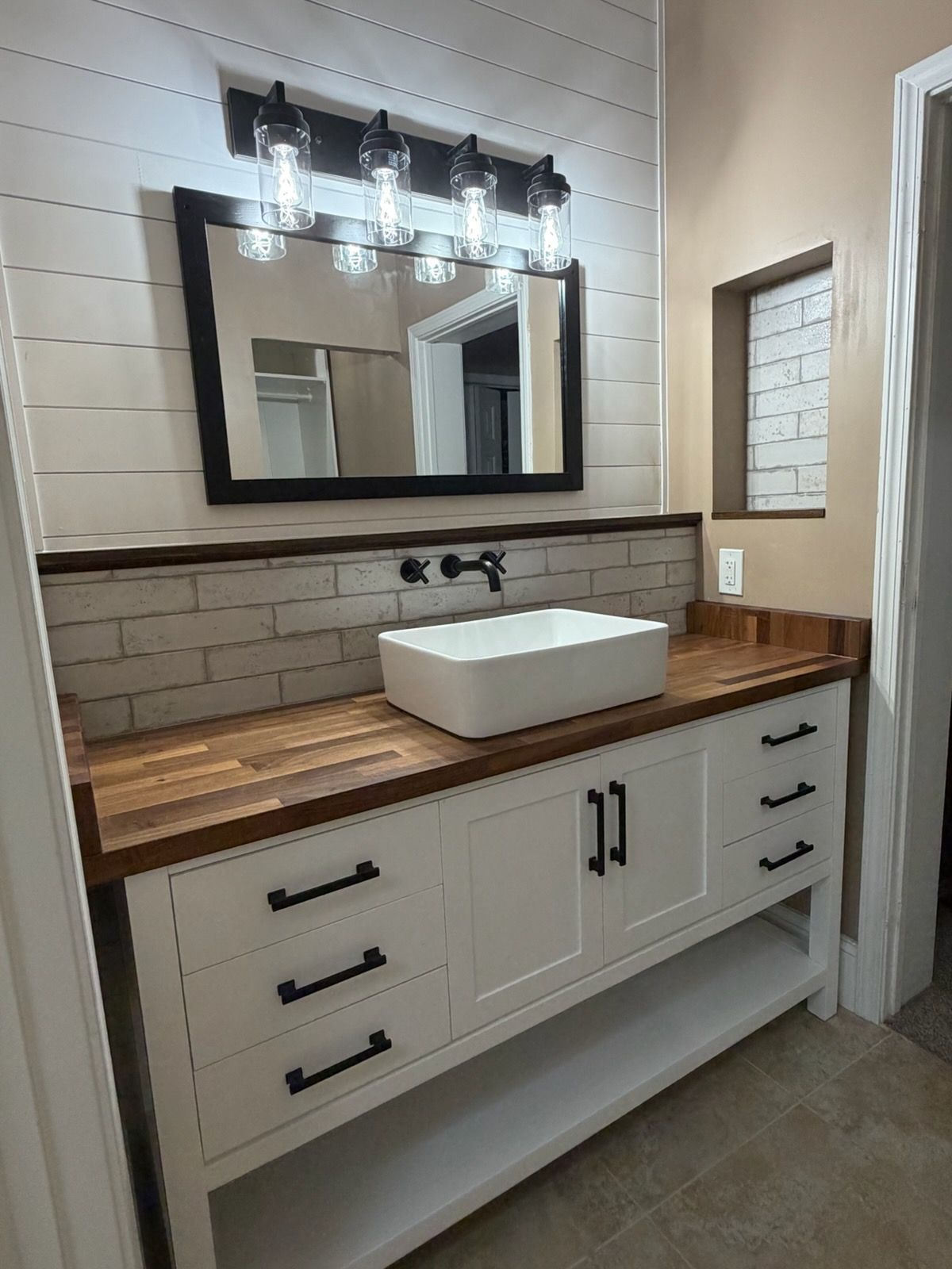 Modern bathroom vanity with white sink, wood countertop, black fixtures, and illuminated mirror