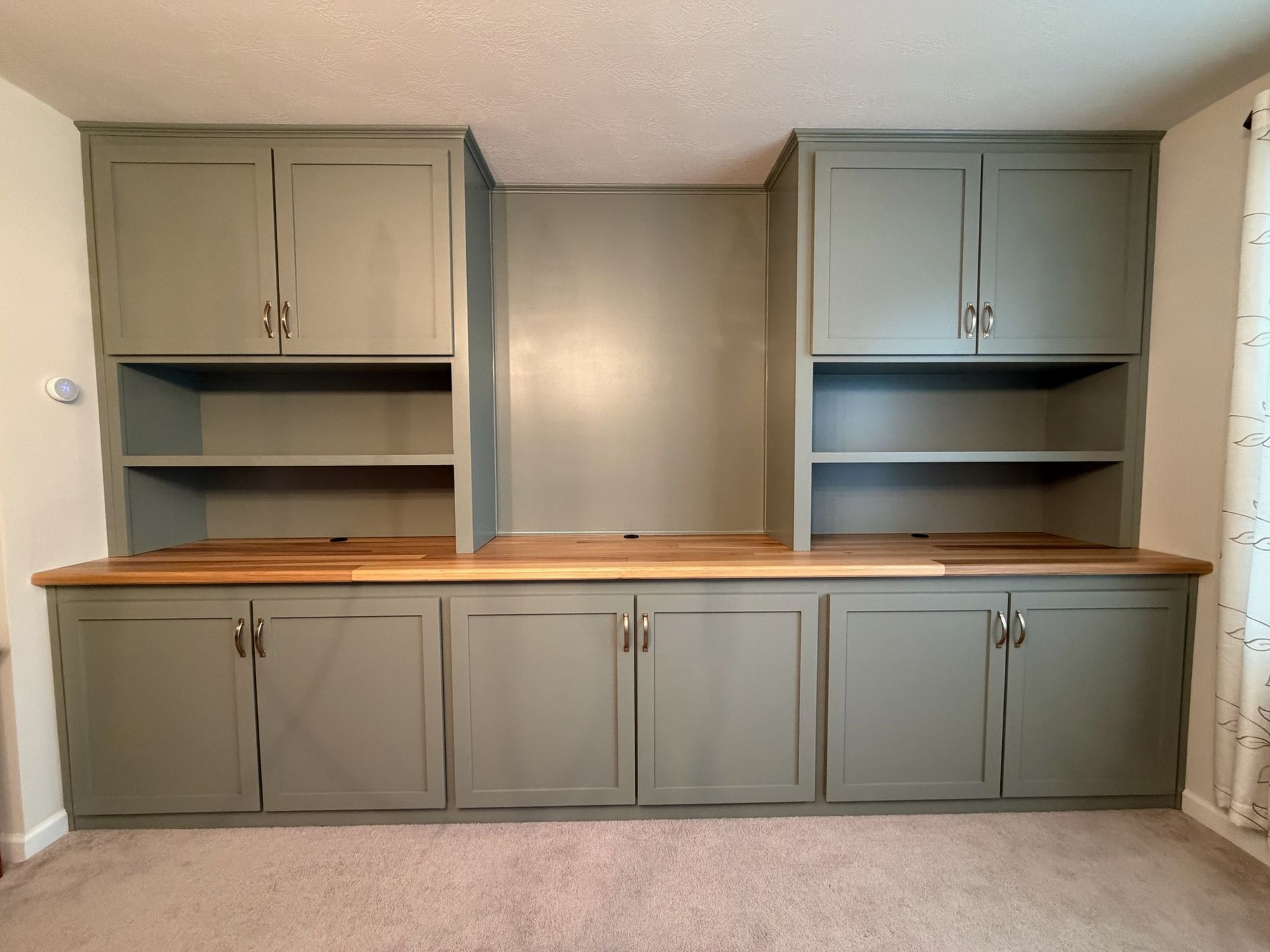 Built-in gray cabinets with wood countertop and open shelves against a beige wall