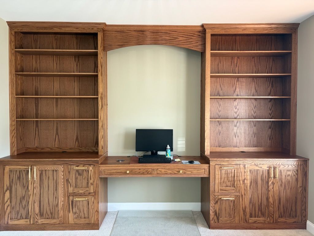 Wooden wall unit with bookshelves, cabinets, and a central desk holding a computer monitor.