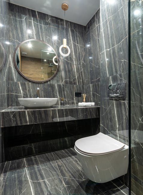 Modern gray tiled bathroom with floating sink, round mirror, and wall-mounted toilet