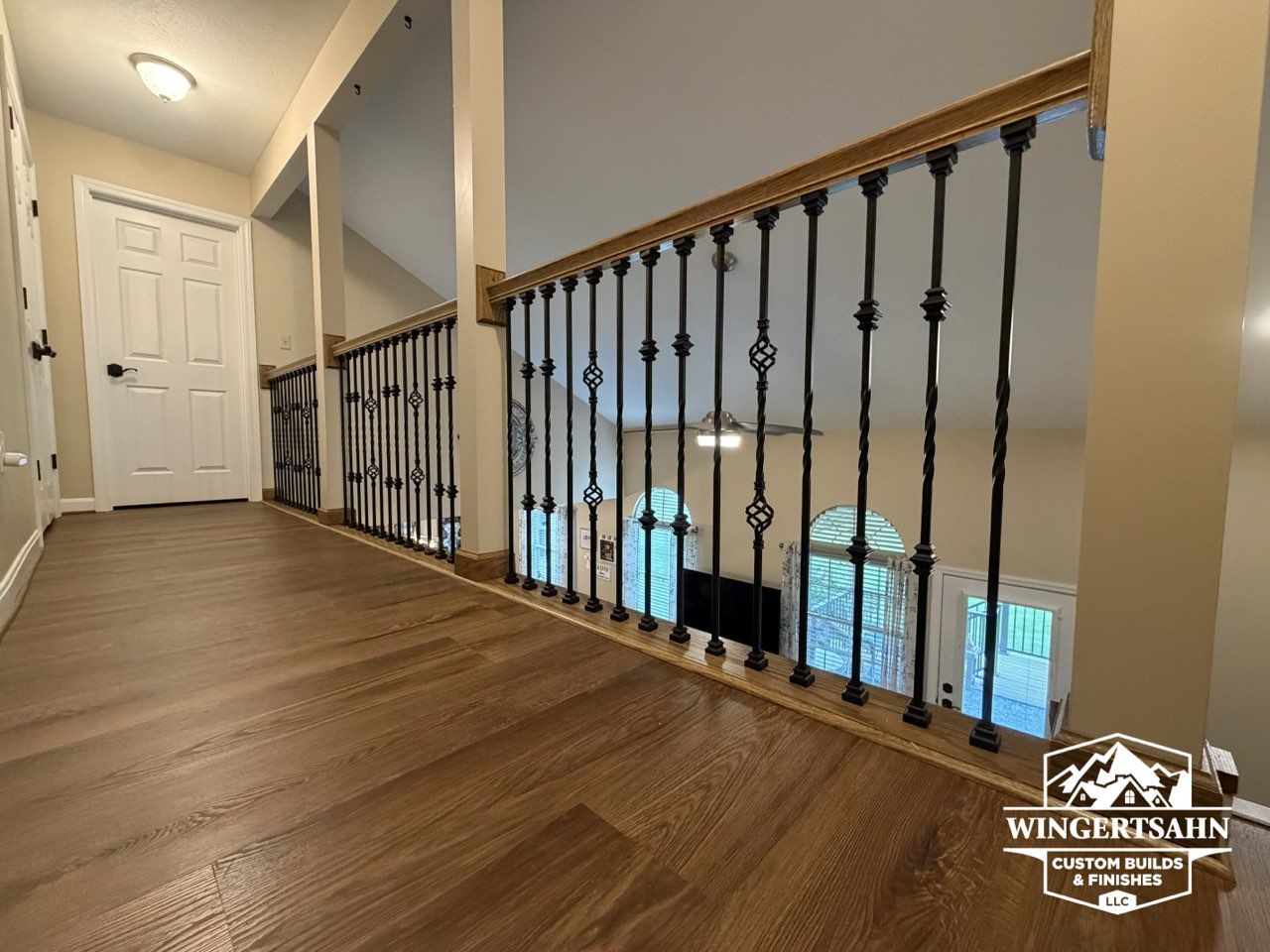 Upper hallway with wood floor, white walls, and black iron railing overlooking a lower level.
