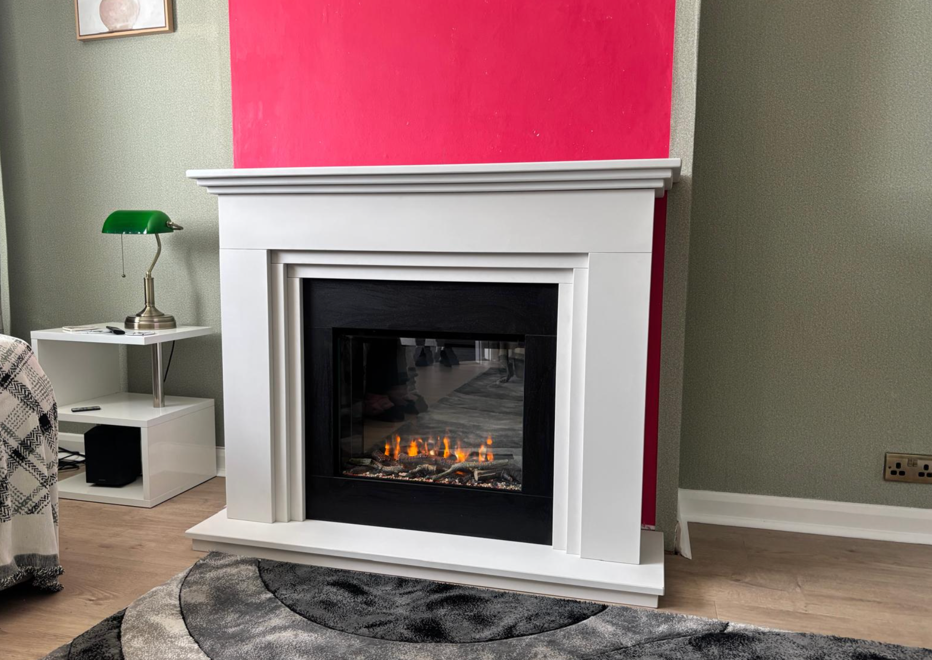 Modern living room with white fireplace, pink accent wall, and a lit fire.