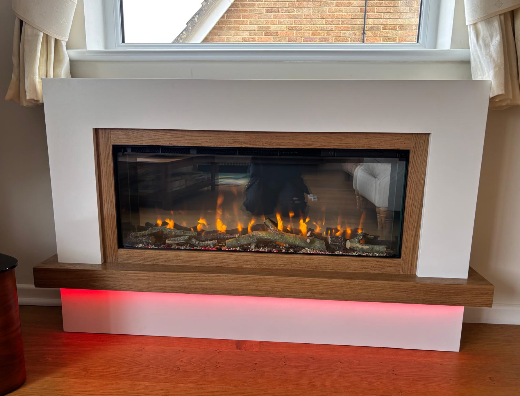 Modern electric fireplace with white surround, wood mantel, and glowing red underlight in a room