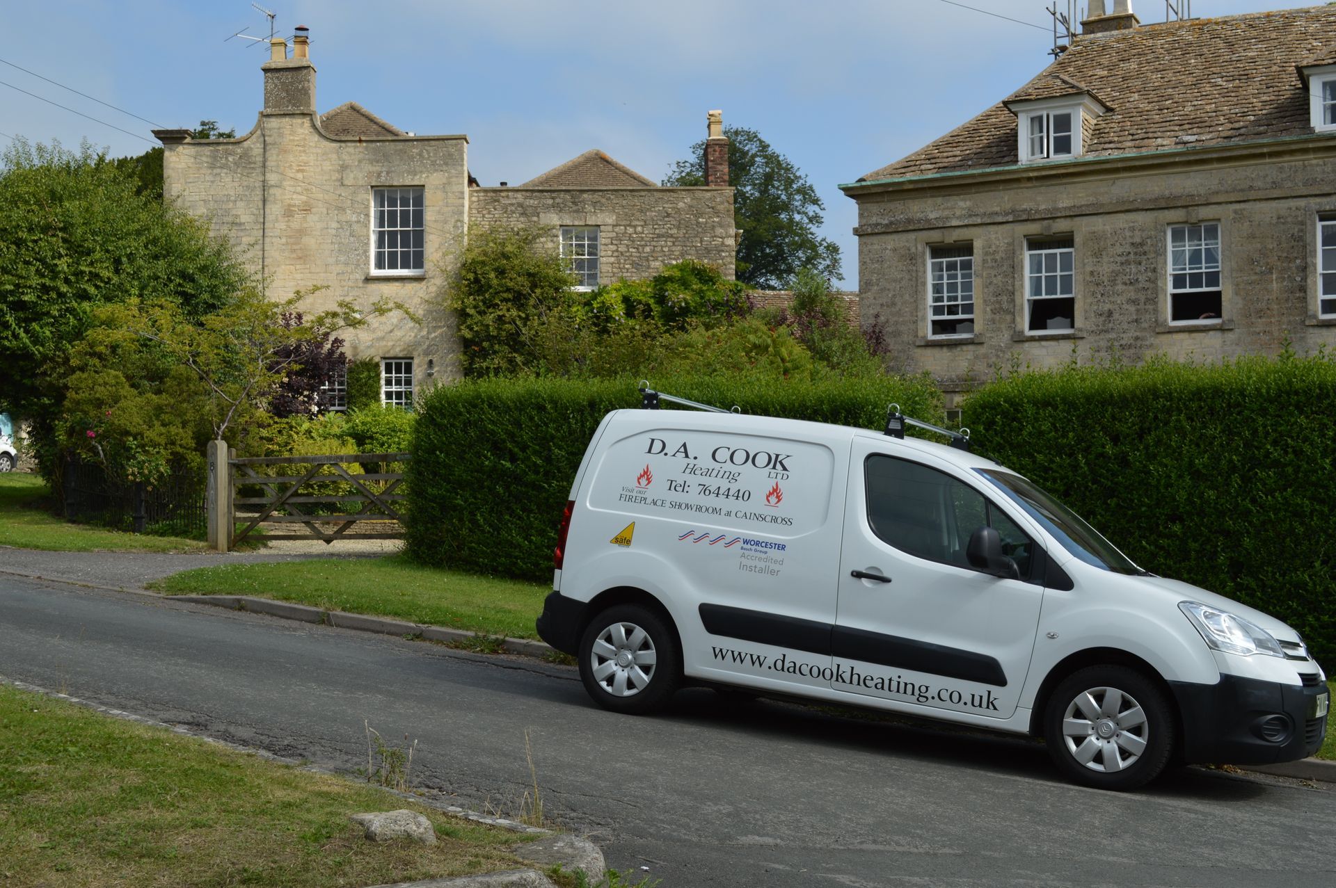 White delivery van parked on a village road beside stone houses and tall green hedges