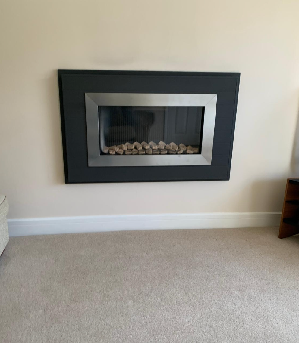 Wall-mounted modern fireplace with black frame and pebbles in a beige room