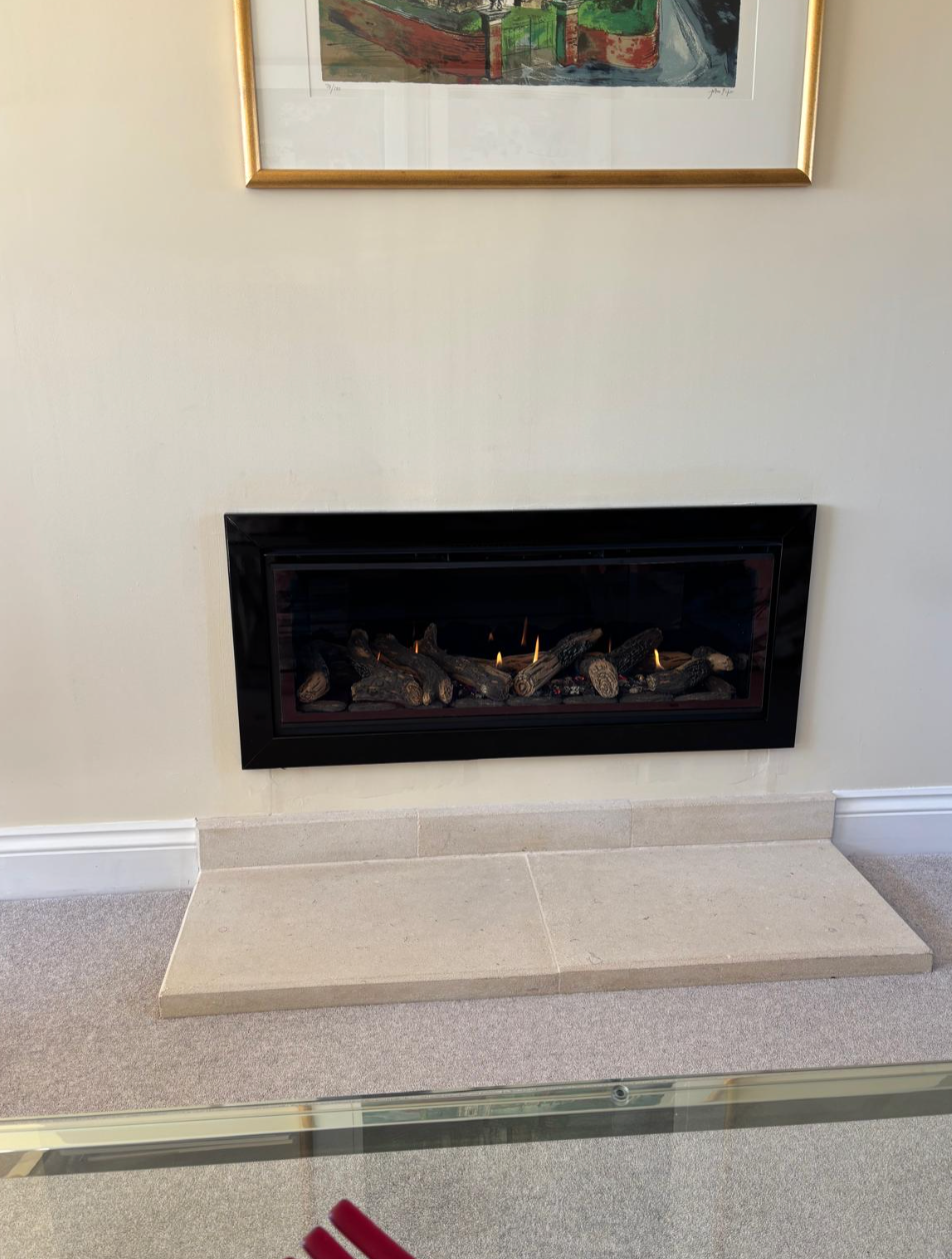 Black rectangular fireplace with cream stone hearth against a white wall in a living room